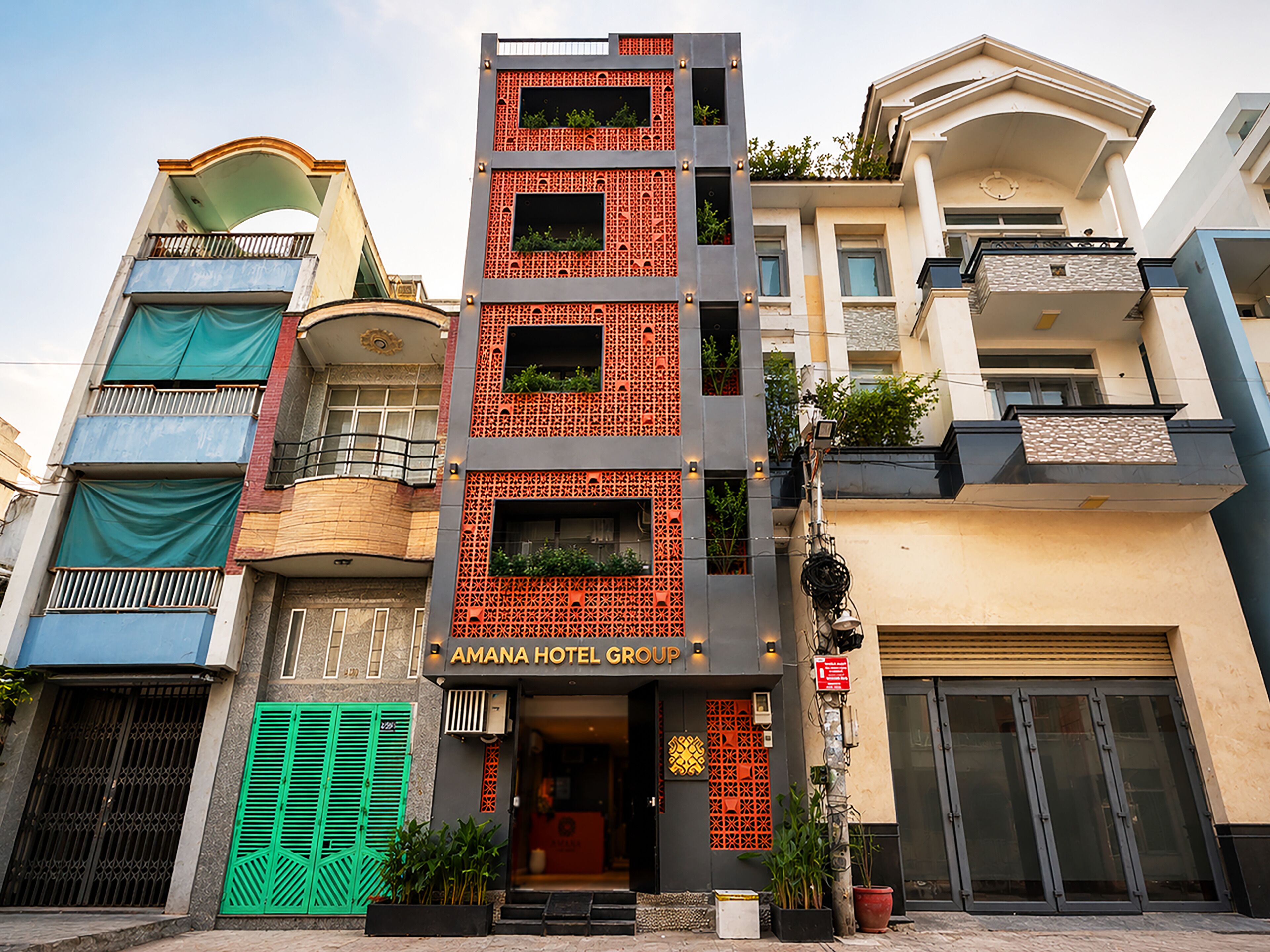 A multi-story hotel with a modern facade, balconies, and visible signage for the 'AMANA HOTEL GROUP'.