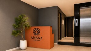 A reception desk with a logo, a potted plant, and a hallway leading to an elevator. - Amana Living - Nguyen Canh Chan (Ho Chi Minh City)