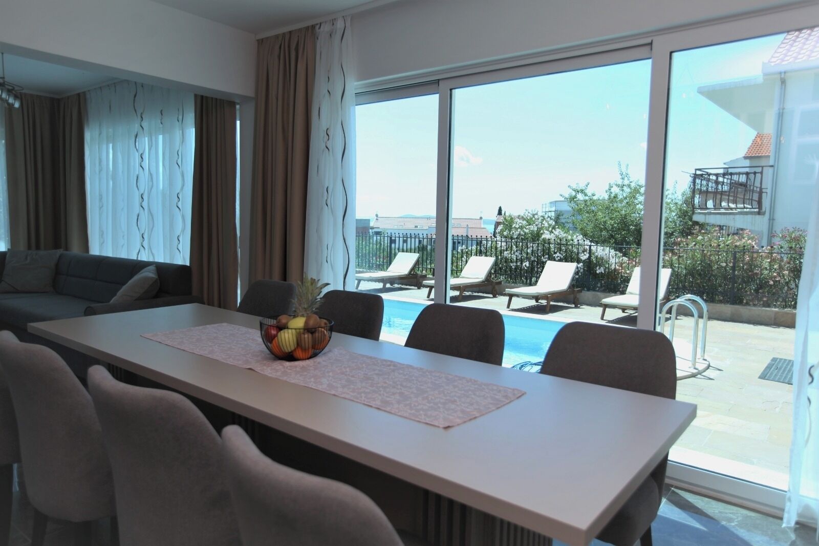 A modern hotel room with a dining area, large windows, and a view of a pool and outdoor seating.