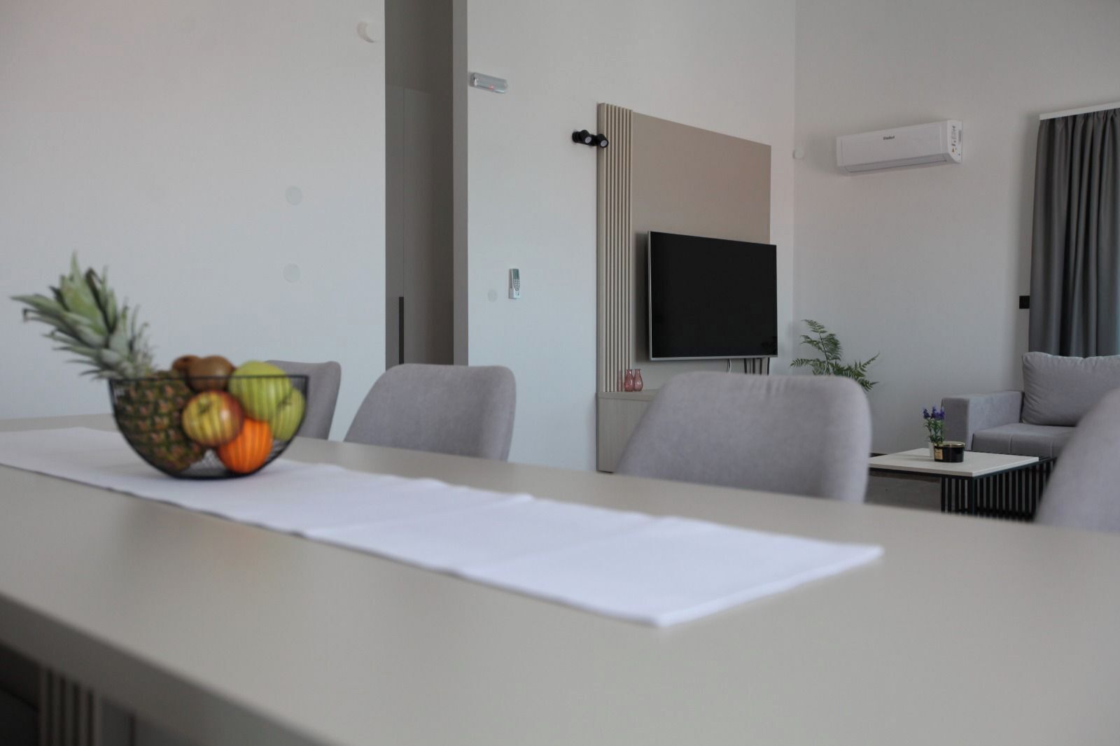 A modern hotel room with a dining table, chairs, a TV, and a small side table with a plant.