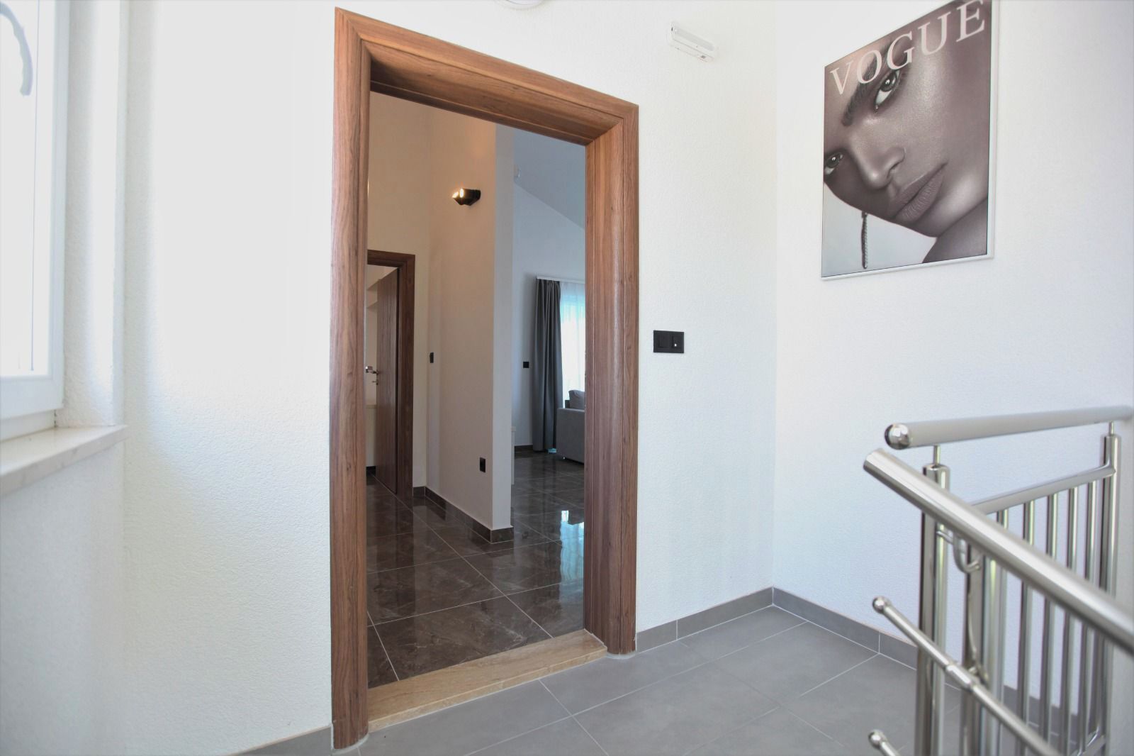 A hallway with a wooden door, a staircase with a metal railing, and a poster on the wall.
