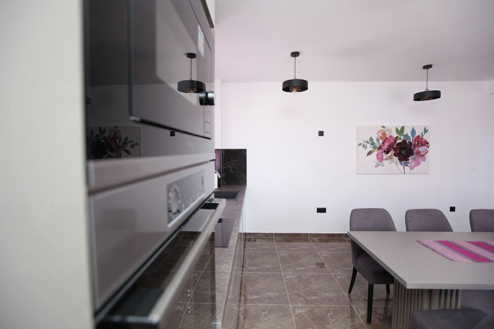 Una cucina moderna con elettrodomestici integrati, un'area pranzo con tavolo e sedie, e un lampadario fissato a parete.