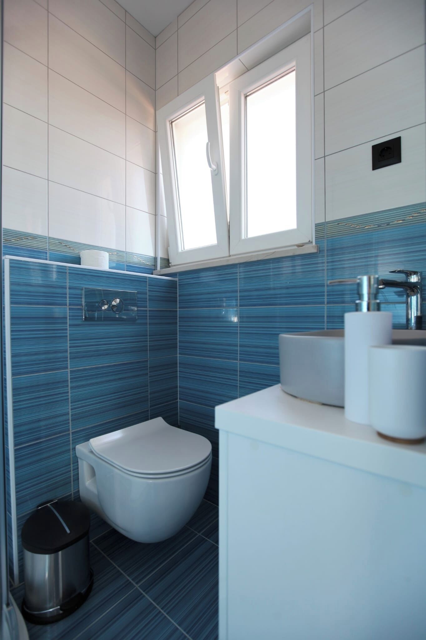 A modern bathroom with a toilet, sink, and window.