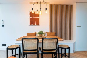 A dining area with a wooden table, four black chairs, a potted plant, and a wall-mounted light fixture. - Superbe 3 pièces Carré d'Or, Parking & Clim (Nice)