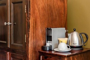 Un mueble de madera con una cafetera, una taza y un hervidor sobre una encimera de madera.