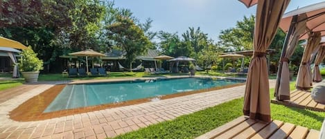 A swimming pool with a tiled deck, surrounded by grass and trees.