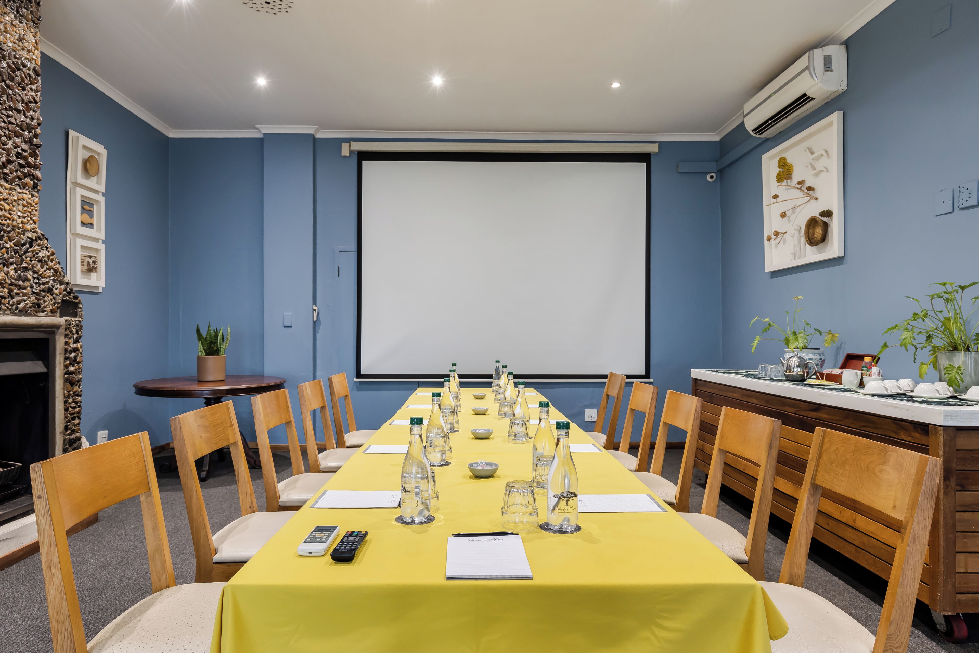 A conference room with a long table, chairs, a projector screen, and a fireplace.