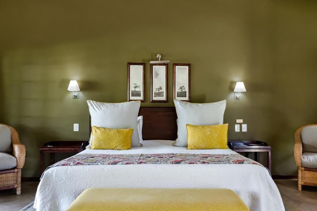 A hotel room with a large bed, two bedside tables, two wall-mounted lamps, and a headboard with three framed pictures.