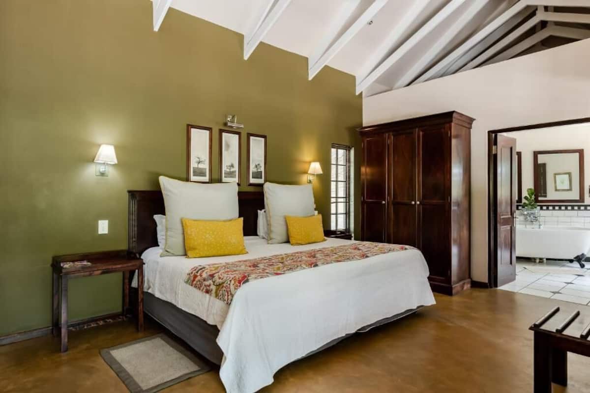A bedroom with a large bed, two bedside tables, a nightstand, a wardrobe, and a bathroom visible through an open door.