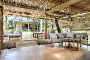 Un área de estar al aire libre con mobiliario de madera y techo de paja.