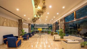 Um lobby moderno com piso de mármore, assentos em azul e bege, e uma grande janela com vista.