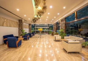 A modern lobby with marble flooring, blue and beige seating, and a large window with a view. - Bloom Boutique | Bangalore Palace Rd. (Bengaluru)