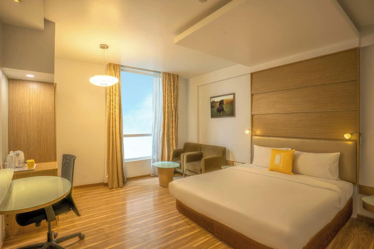 Una habitación de hotel con cama, escritorio, silla, mesita y ventana con cortinas.