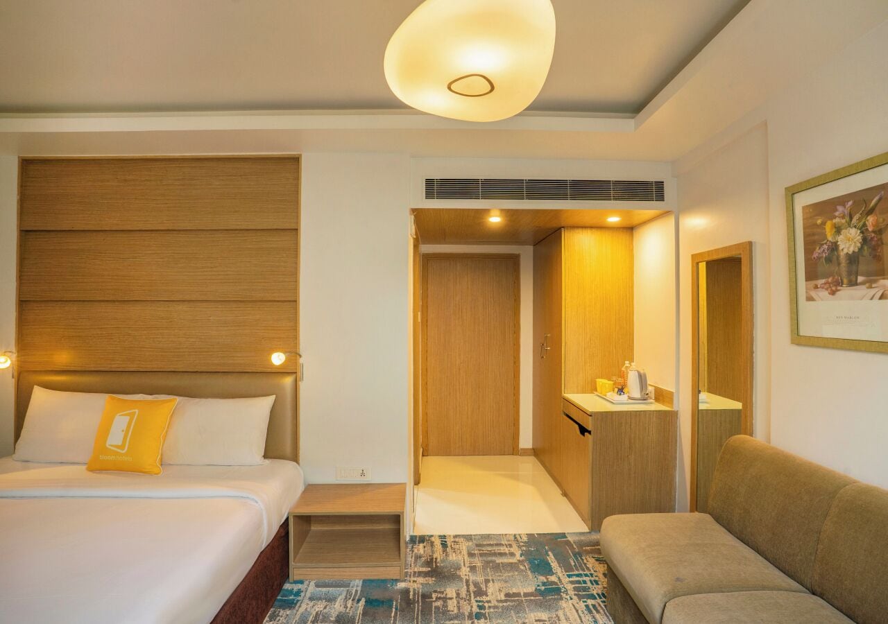A hotel room with a bed, a sofa, a small table with a lamp, and a door leading to a bathroom.