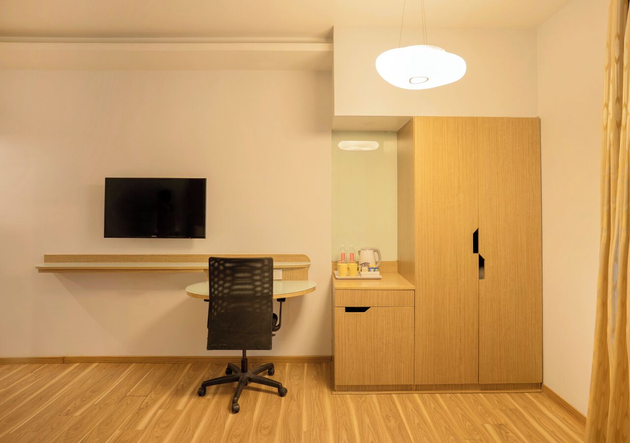 A compact room with a desk, chair, television, wardrobe, and a small table with items.