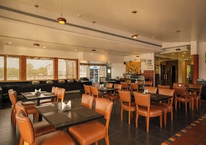 A spacious restaurant with high tables and chairs, a bar area, and a seating section with cushioned benches. - Bloom Boutique | Bangalore Palace Rd. (Bengaluru)