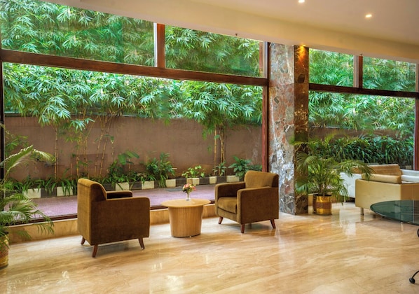 A spacious room with large windows, a sofa, armchairs, and a coffee table. - Bloom Boutique | Bangalore Palace Rd. (Bengaluru)