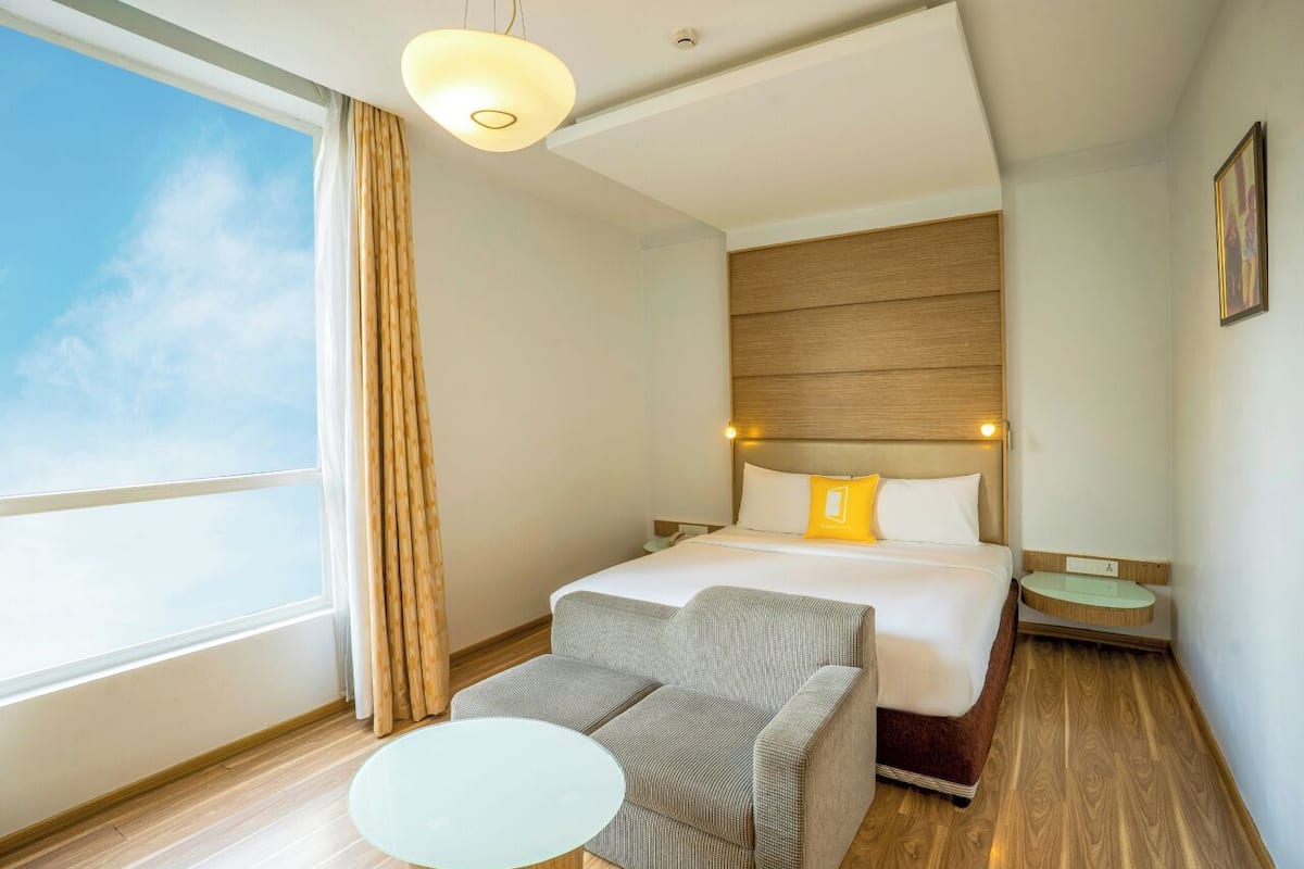 Habitación de hotel con cama, sofá, mesita, mesita de noche y ventana con cortinas.
