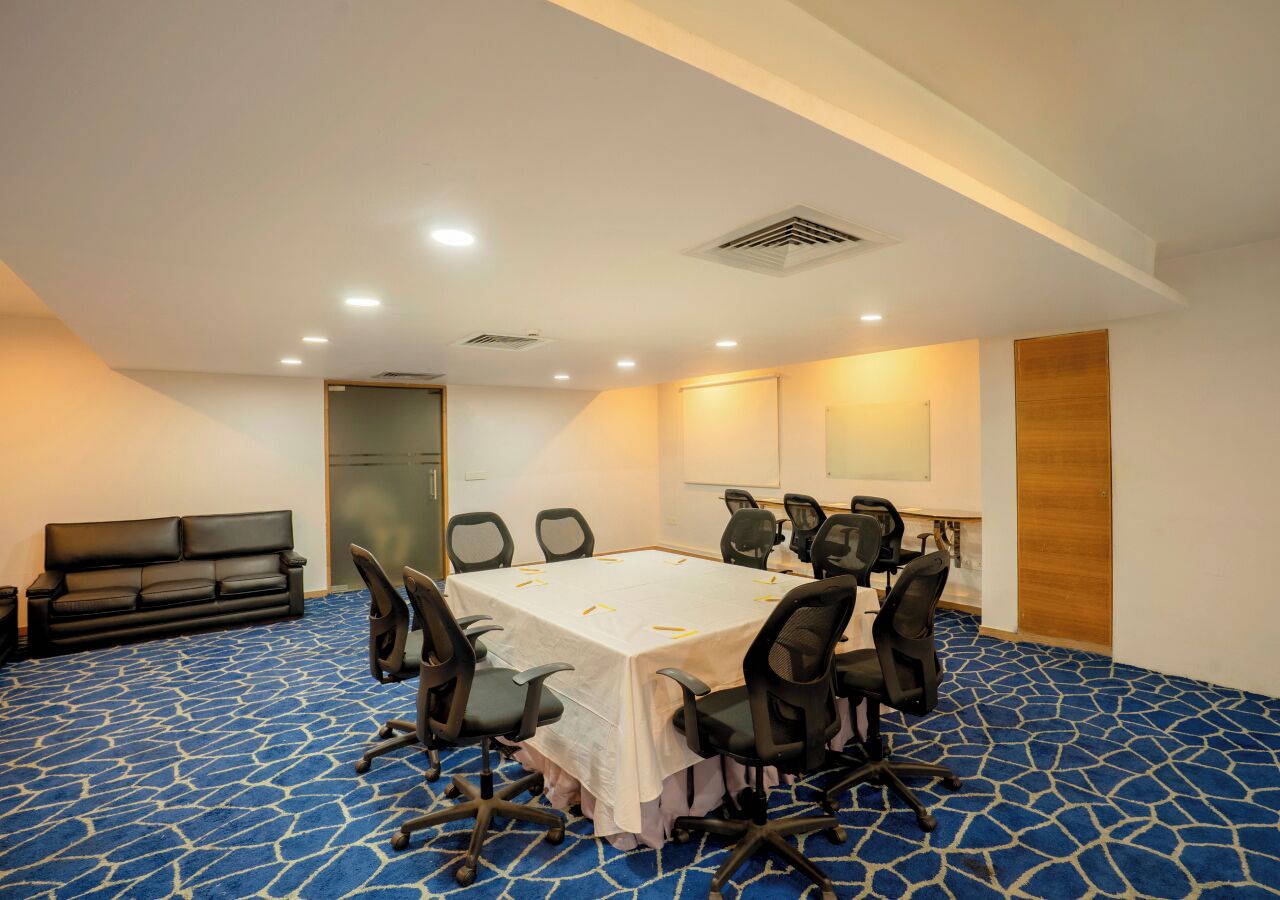 A conference room with a long table, multiple chairs, a sofa, and a patterned carpet.