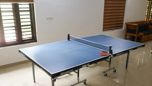Een tafeltennistafel met wielen, een houten stoel en een raam met jaloezieën.