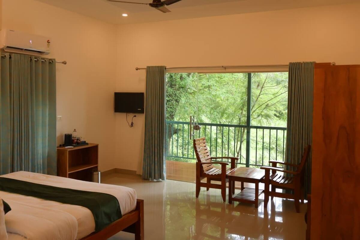 Habitación de hotel con cama, una mesa de madera con sillas, televisión y balcón con cortinas.