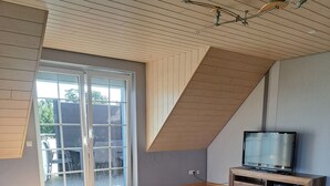 Ett modernt vardagsrum med en stor blå soffa, ett soffbord, en tv på ett träställ och en skjutdörr i glas som leder ut till ett utomhusområde.