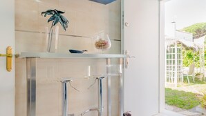 Ett modernt badrum med en duschkabin i glas, en handduksställning, en krukväxt och ett litet bord med en skål och ett glas.