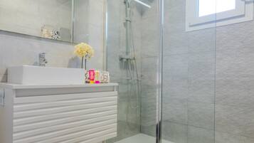 A modern bathroom with a glass shower enclosure, a white vanity with a mirror, and a small vase of flowers.