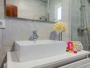 A bathroom with a white sink, a mirror, a shower, and toiletries on a shelf. - Villa Vieira in Chiclana de la Frontera (Chiclana de la Frontera)