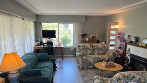 A living room with a sofa, a chair, a desk with a computer, a lamp, and a fireplace. - Enjoyable 3-bedroom house in charming Surrey neighborhood, close to everything (Surrey)