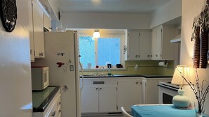 A compact kitchen with white cabinets, a window, and a dining area with a table and chairs. - Enjoyable 3-bedroom house in charming Surrey neighborhood, close to everything (Surrey)