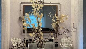 A room with a large window, a television, two white wicker chairs, and decorative branches in vases. - Enjoyable 3-bedroom house in charming Surrey neighborhood, close to everything (Surrey)