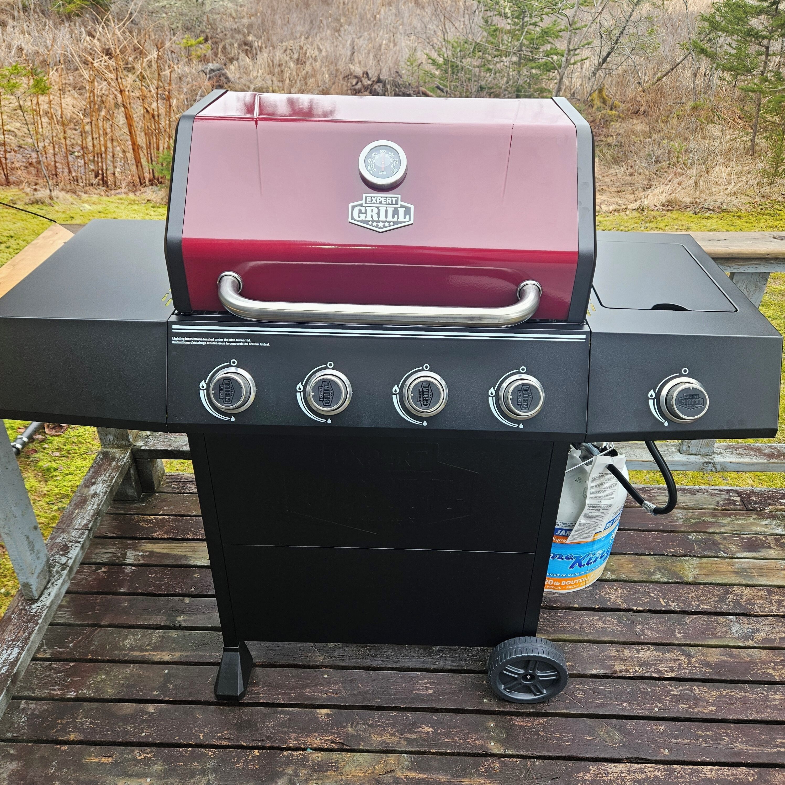 Una parrilla con cuatro perillas de control, un asa y una rueda para facilitar su movimiento.