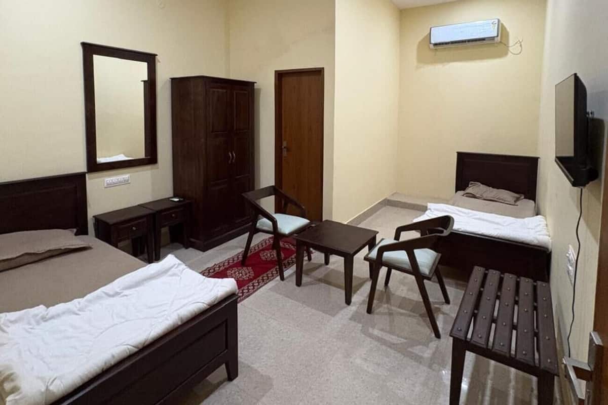 A hotel room with a bed, a desk, a chair, a small table, a wardrobe, a television, and an air conditioning unit.