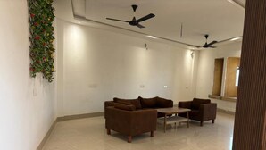 A spacious room with a brown sofa set, a small table, and ceiling fans. - Hotel Bhargav Palace (Jaisalmer)