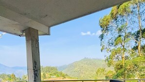 A glass-top table with four chairs on a balcony with a view of hills and trees. - Star Place Homestays (Kodaikanal)