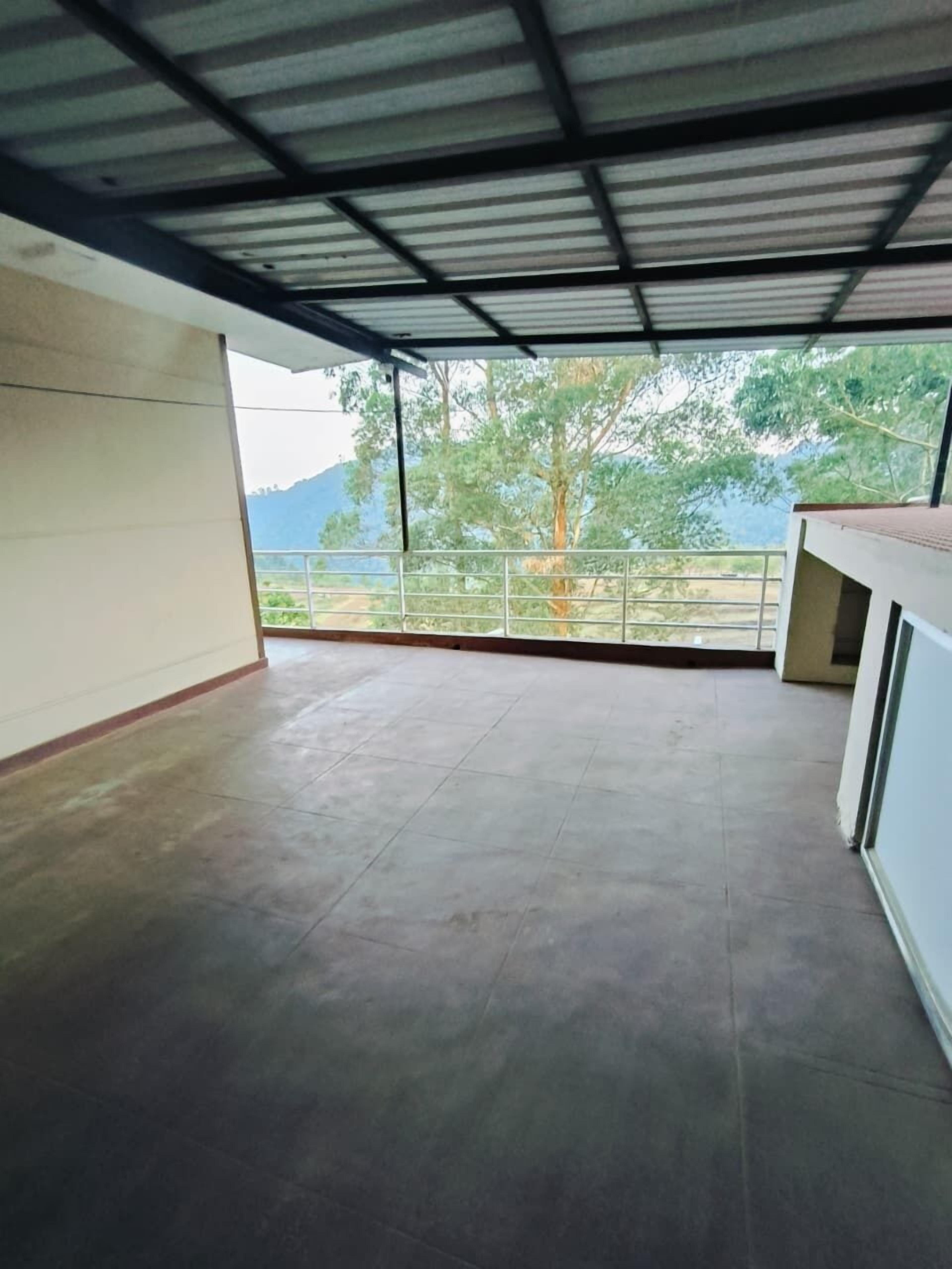 A spacious room with a tiled floor, a balcony with a metal railing, and a view of trees and mountains.