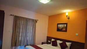A hotel room with a bed, a nightstand, a wall-mounted lamp, and a painting. - Star Place Homestays (Kodaikanal)