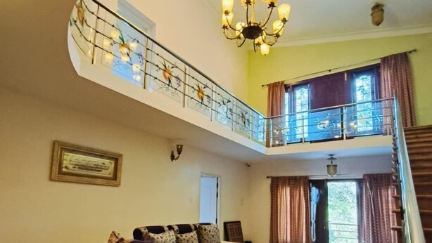 A spacious living area with a sofa set, a chandelier, a staircase, and a balcony with a railing. - Star Place Homestays (Kodaikanal)