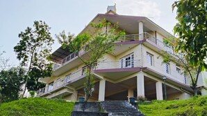 A multi-story building with a balcony, stairs leading up to the entrance, and a grassy hill in the foreground. - Star Place Homestays (Kodaikanal)