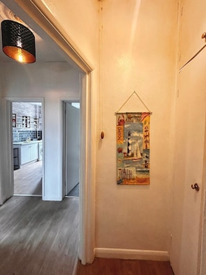 Un couloir avec une porte, une œuvre d’art accrochée au mur et une cuisine visible à travers une porte ouverte.