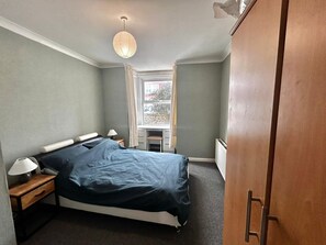 Une chambre à coucher comprenant un lit, des tables de chevet, une fenêtre avec des rideaux, un radiateur et une armoire.