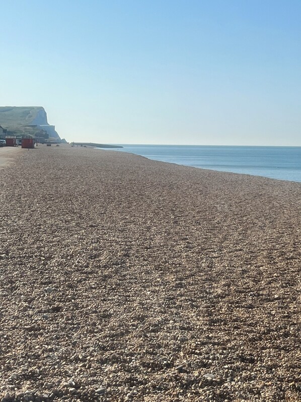 A pebbled beach with a clear sky and a distant cliff.