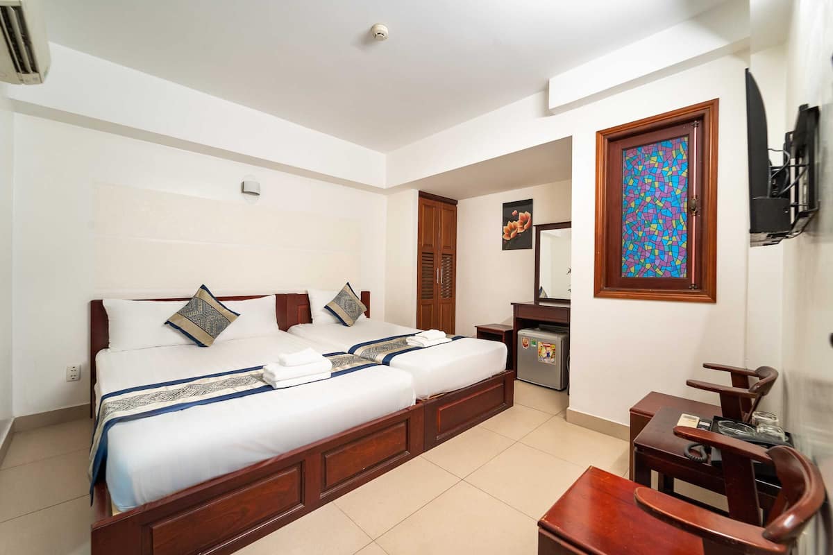 A hotel room with a large bed, a desk, a chair, a TV, and a small refrigerator.