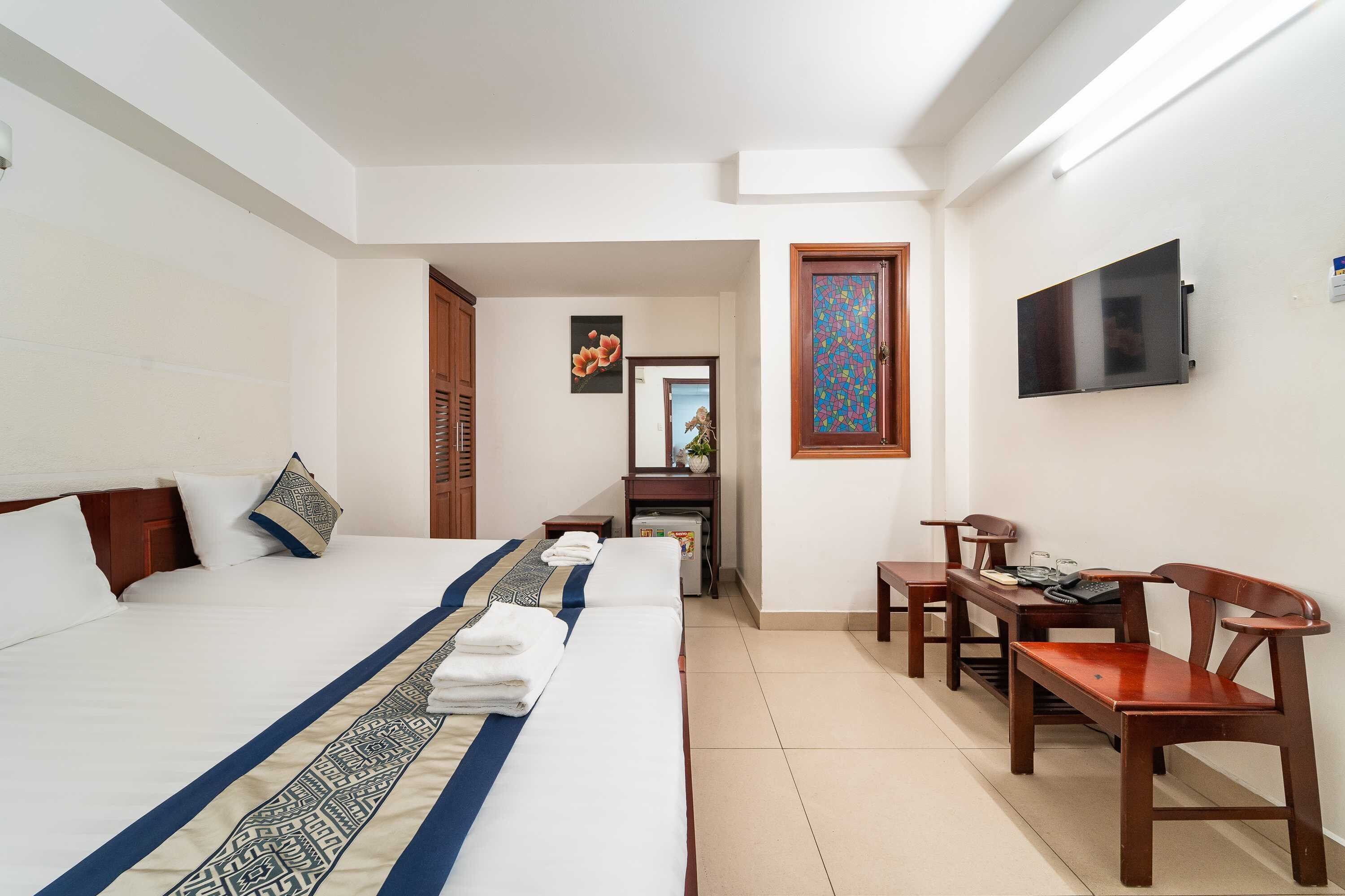 Una camera d'albergo con un letto grande, una scrivania con una sedia, una televisione a parete e un tavolino con una poltrona.