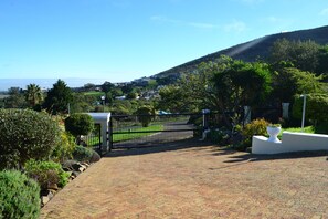 A paved pathway leading to a gated entrance with a view of a green landscape and distant hills. - Accessible City Retreat with Stunning Views and Pool Access (City of Cape Town Metropolitan Municipality)