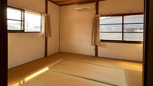 A room with tatami flooring, wooden beams, a ceiling fan, and two windows with curtains. - 60 seconds to the ocean. Just one train ride from Fukuoka Airport. Old-fashioned Japan—something you can't experience at a hotel. Entire traditional Japanese house for rent. (糸島市)