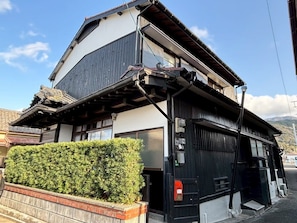 Un edificio japonés tradicional de dos pisos con exterior blanco y negro y un pequeño jardín con arbustos bien cuidados.