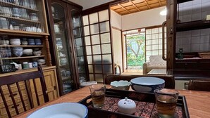 A traditional Japanese dining room with a wooden table set for a meal, a tea set, and a view of a garden through a sliding door. - 60 seconds to the ocean. Just one train ride from Fukuoka Airport. Old-fashioned Japan—something you can't experience at a hotel. Entire traditional Japanese house for rent. (糸島市)