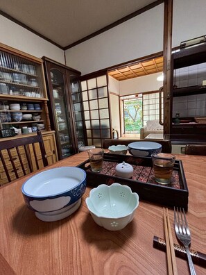 Un comedor japonés tradicional con una mesa de madera dispuesta para una comida, un juego de té y vistas a un jardín a través de un puertas correderas.